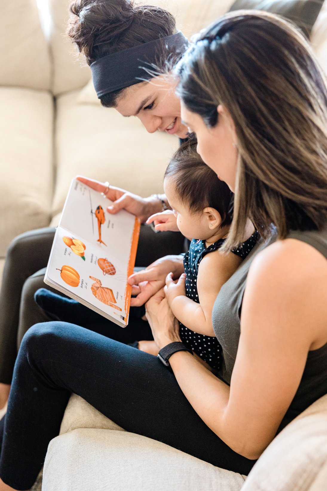 LGBT Couple with Baby Reading a Book on Sofa